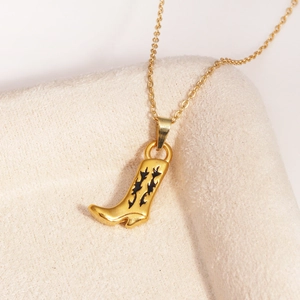 Détail macro du pendentif botte de cow-boy doré avec motifs en émail noir sur tissu