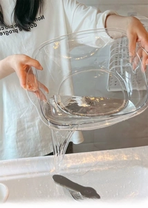 Deep transparent washbasin with wide rim shown pouring water in a modern sink