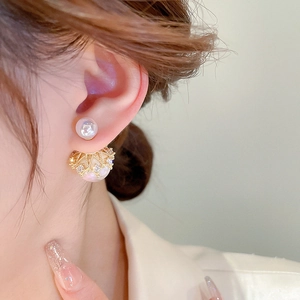 Detail of crown-shaped gold earrings with iridescent pearls and diamonds on earlobe