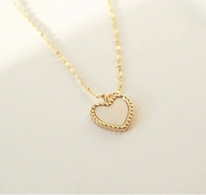 Detailed close-up of a white heart-shaped shell pendant with gold beaded edges on a chain