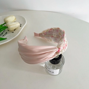Detail of pink satin headband with floral lace knot on a white surface with tulips