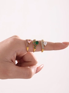 Dettaglio di tre anelli a cuore placcati in oro con smalti di colore rosa, verde e bianco