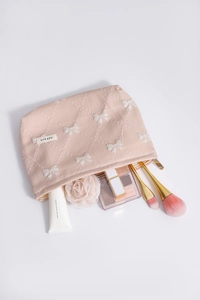 Dettaglio del beauty case rosa con ricami a fiocco bianco e trama trapuntata a griglia