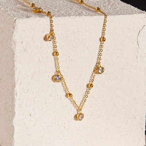 Detail of a gold bead chain necklace with bezel-set clear round stones on a display block