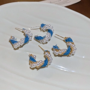 Detailed view of C-shaped denim and pearl wrapped hoop earrings on a textured plate