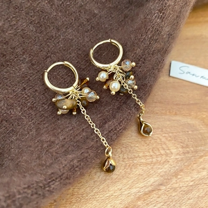 Detail von goldenen Quastenohrringen mit Tigerauge, Perlen und Bernsteinperlen auf Pullover