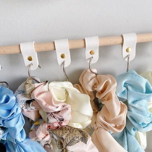 Detail of colorful silk scrunchies hanging on white PU leather hooks with metal clips