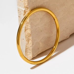 Minimalist gold-plated stainless steel solid bangle on a textured beige stone base