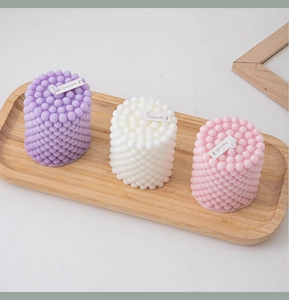 Close-up of geometric bubble candles in purple, white, and pink on a wooden tray