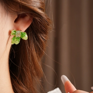 Detail of gold-plated flower earrings with green stones worn on ear for aesthetic style