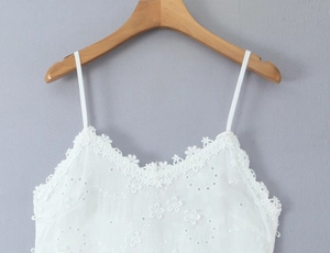 Détail d'un caraco blanc avec broderie florale délicate et bordures en dentelle fine