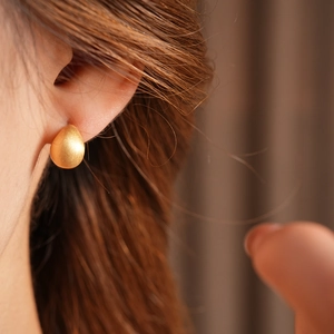 Close-up of a brushed gold water drop earring worn on ear with professional soft lighting