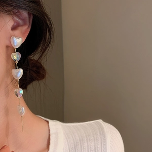 Detail of elegant gold chain earrings with pearl and iridescent heart-shaped pendants