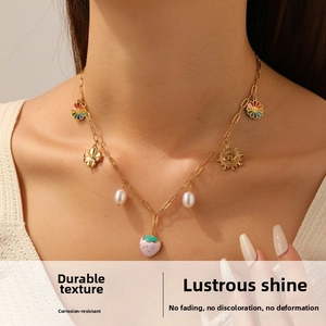 Close-up of gold necklace with strawberry, pearl, and sunflower charms on a model