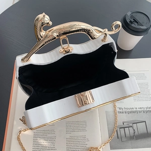 White textured handbag with unique gold leopard handle and elegant chain strap on a table