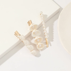 Detailed view of three golden hairpins with white pearls and natural shells on white decor