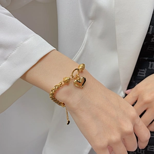 Gold stainless steel heart pendant bracelet on wrist with elegant white suit background