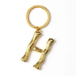 Close-up of a gold metal letter H keychain with a circular ring on a white background