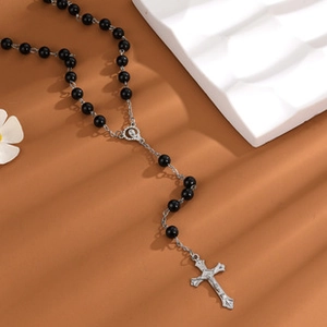 Détail du collier croix en métal argenté avec perles noires de style rosaire sur fond brun