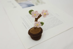 Detail of a handmade crochet potted plant featuring pink flowers and green leaves on a book