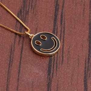 Macro shot of gold necklace featuring black round smiley face pendant on brown texture