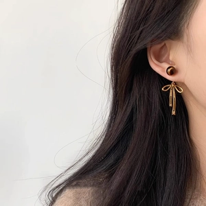Close-up of golden bow earrings with tiger eye stone beads on a female model