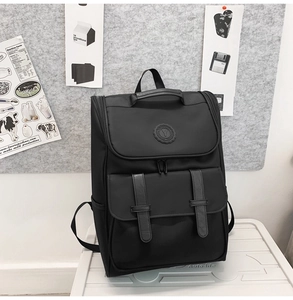 Detail of a black nylon backpack featuring front flap pockets and leather buckle straps