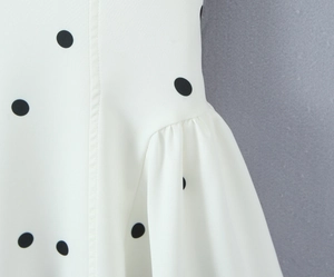 Détail du tissu blanc à pois noirs montrant des plis souples et la texture de couture