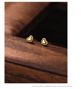 Macro detail of gold heart-shaped stud earrings with delicate beaded edge and silver base