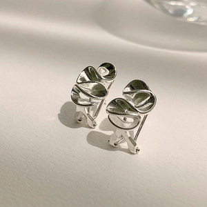 Macro shot of silver wave earrings showing high-polish finish and fluid metallic design