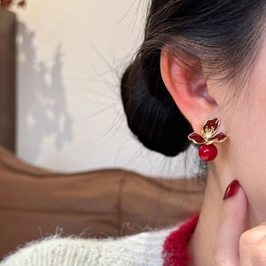 Boucles d'oreilles fleur rouge vintage avec perle et bordure dorée portées par un mannequin