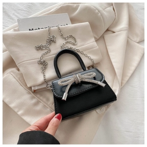 Close-up of black crossbody bag with silver rhinestone bow on beige blazer