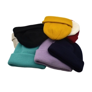 Collection of thick knitted beanies in multiple colors stacked on a white background