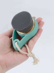 Close-up of mint green facial brush with gold ring detail and hanging cotton rope