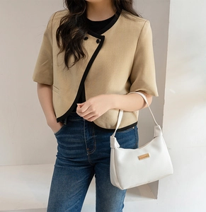 Close-up of a white lychee grain half-moon underarm bag held by a model in a beige jacket