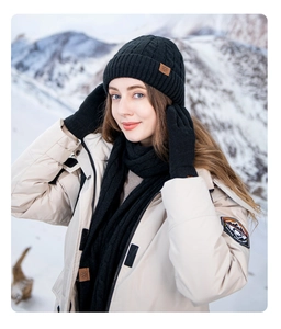 Close-up of black winter knitted hat and scarf set with snow leather patch in snowy landscape