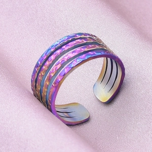 Macro shot of rainbow titanium steel open ring with textured lines on pink fabric