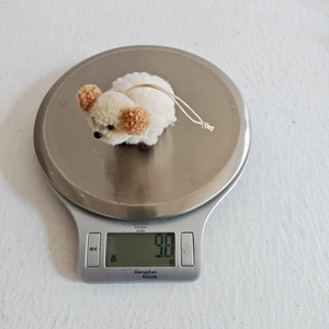 Detail shot showing the lightweight 9.8g white wool felt dog ornament on a digital scale