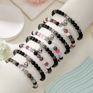 Close-up of seven natural stone beaded bracelets with heart pendants on a display stand