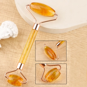 Macro detail of amber resin facial roller showing dual smooth massage heads and gold frame
