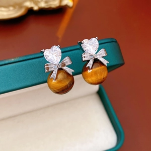 Detail of silver bow earrings with heart-shaped zircon and tiger eye stone bead