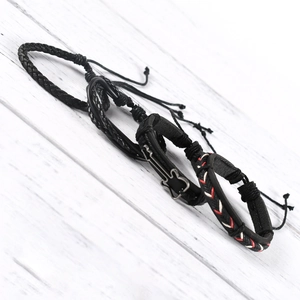 Three-piece black woven leather bracelet set with silver heart and key charms on white wood