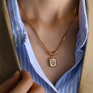 Detail of gold snake chain with heart zircon pendant worn over a classic striped shirt