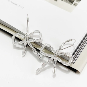 Macro detail of 925 silver bow earrings with rectangular zircon stones on white paper