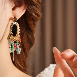 Close-up of golden leaf tassel earrings with red and green beads on a female model