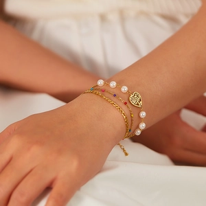 Detailed view of multilayered gold chain bracelet with pearls and heart charm