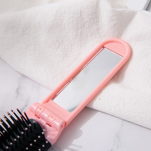 Pink foldable 2-in-1 hairbrush with mirror and massage bristles on marble surface