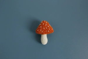 Macro shot of handmade crochet mushroom brooch featuring orange cap and white details