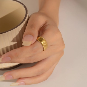 Close-up of a gold wavy textured ring worn by a model holding a ceramic cup