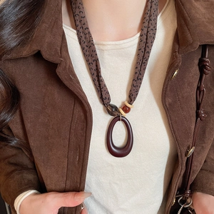 Close-up of leopard print fabric necklace with oval wooden pendant on brown corduroy